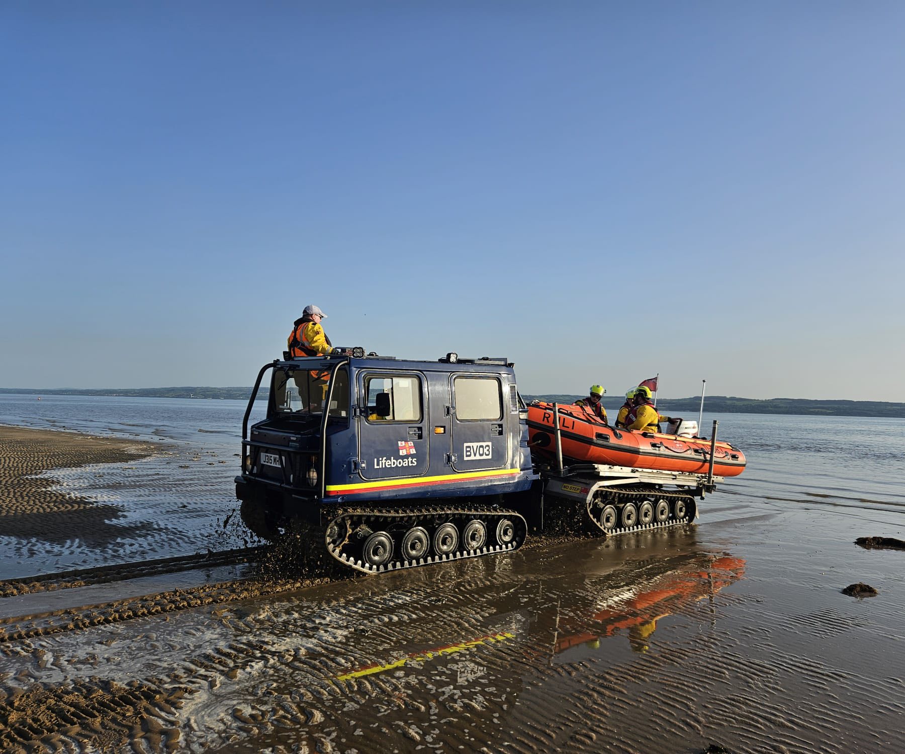 RNLI Hoylake hovercraft BV03 on the sand with a D-class inshore lifeboat embarked on its deck, crew in yellow drysuits