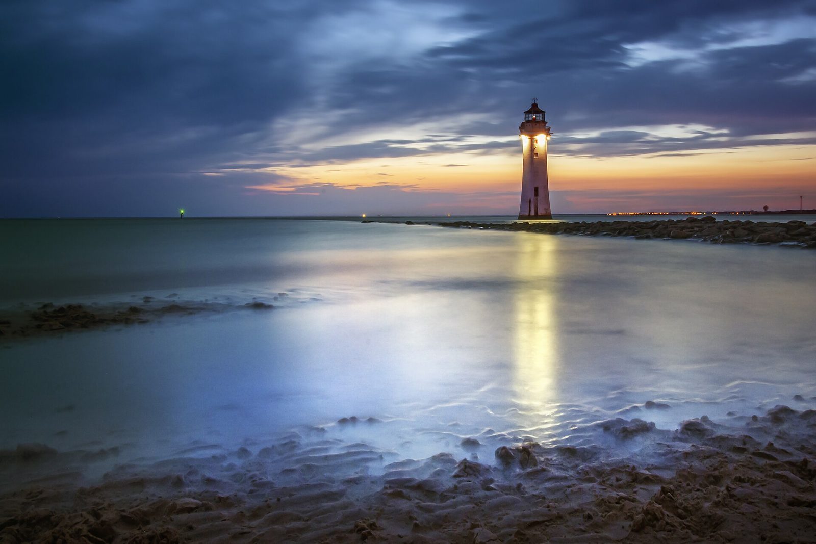 Perch Rock lighthouse at New Brighton at dusk, its beacon lit, reflected in the wet sand at the mouth of the Mersey