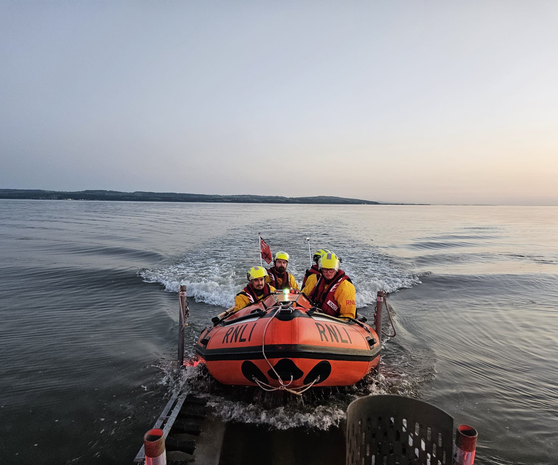 West Kirby RNLI D-class lifeboat with three crew launching from the slipway at dusk into the Dee Estuary