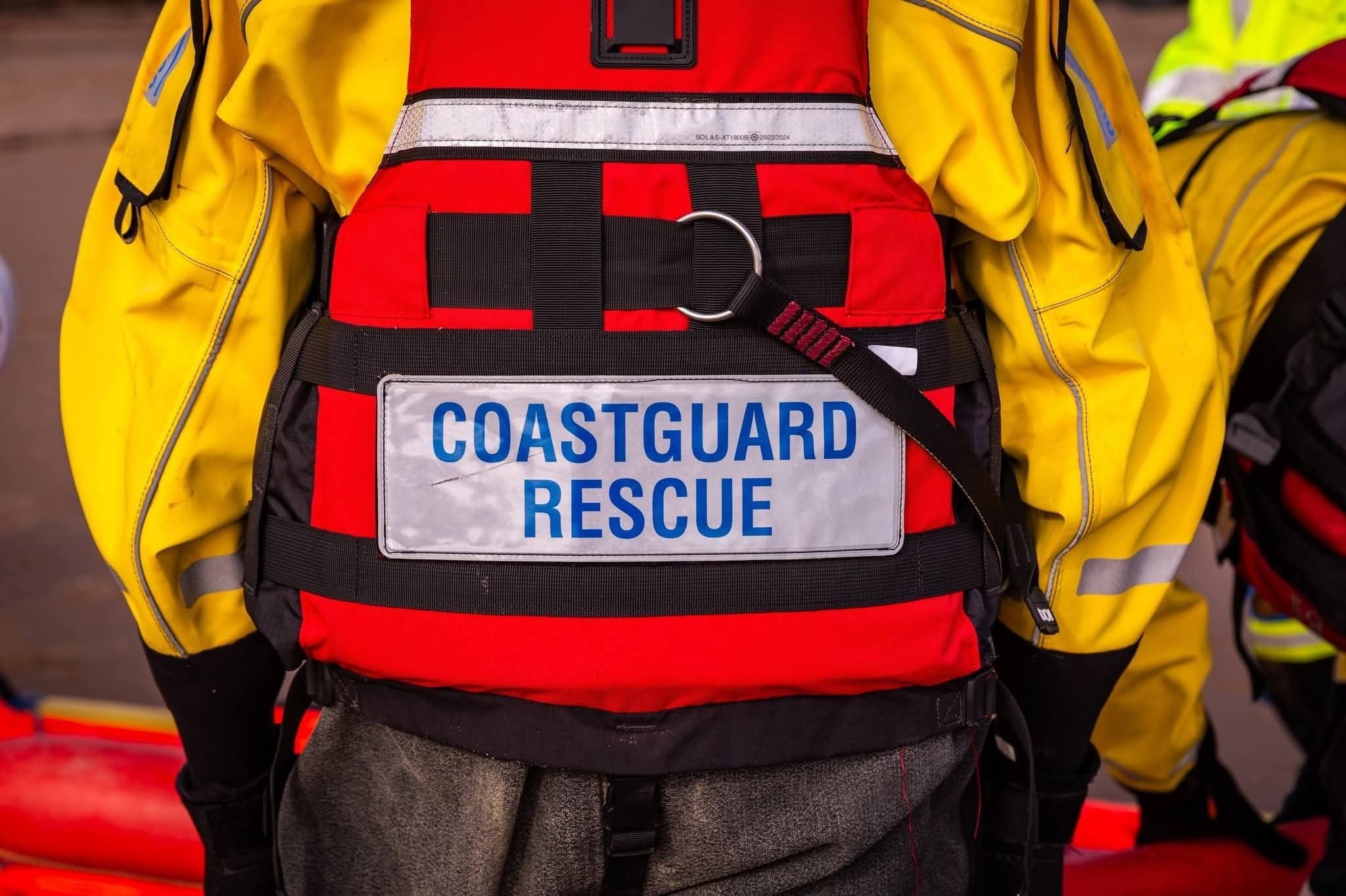 Close-up of a Wirral Coastguard Rescue Officer's red PFD with Coastguard Rescue label, worn over a yellow drysuit