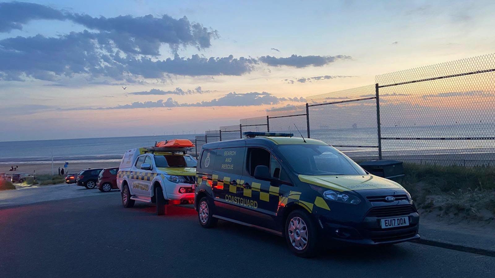 Two HM Coastguard vehicles parked along the Wirral promenade at dusk, with the beach and the sea beyond